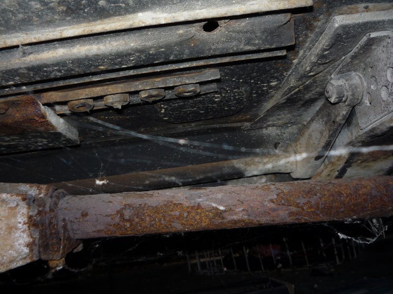 Underside of a vehicle showing rusty exhaust pipe and frame components with some cobwebs