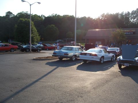 1971 Ford Ranchero - Multiple vehicles are parked in a lot outside a building during the day.
