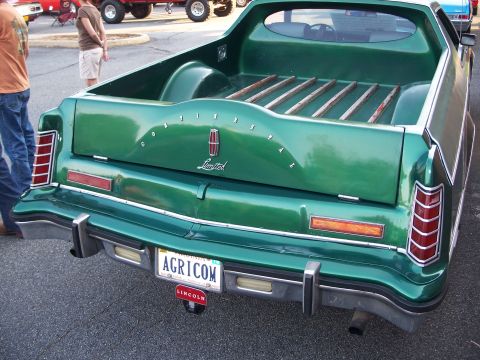 1971 Ford Ranchero - This green pickup truck features Lincoln badging and a wood-slatted bed, with other vehicles visible in the background.