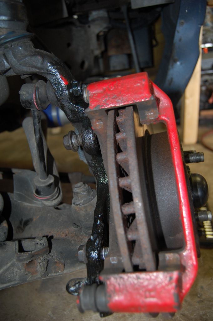 Red brake caliper over a vented rotor, with suspension components visible