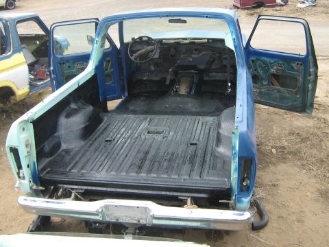 1978 Ford Bronco - The interior of a blue pickup truck is visible with its doors open, showing a stripped-down cabin and bed.