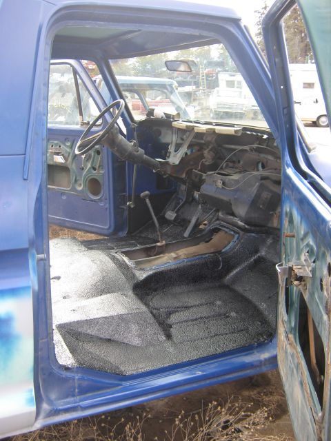 1978 Ford Bronco - The interior of a blue truck is shown with the doors open, revealing a stripped-down dashboard and floor.