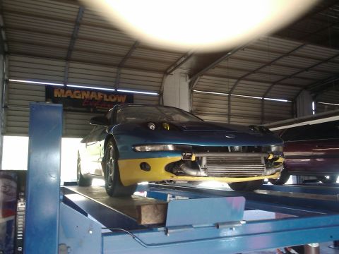 1995 Ford Probe - A modified blue and yellow car is positioned on a vehicle lift inside a garage, with another car visible behind it.