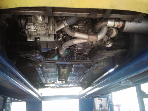 1995 Ford Probe - The underside of a vehicle reveals a complex supercharger setup and custom exhaust piping.