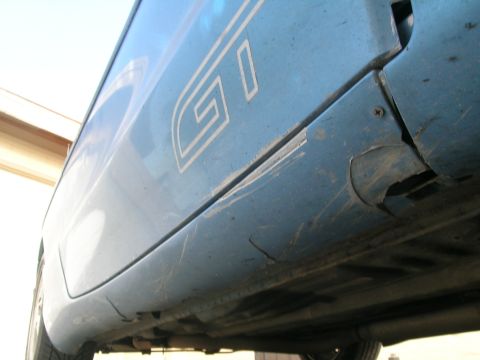 1995 Ford Probe - Close-up of a blue car's side panel showing a GT emblem and signs of wear and tear.