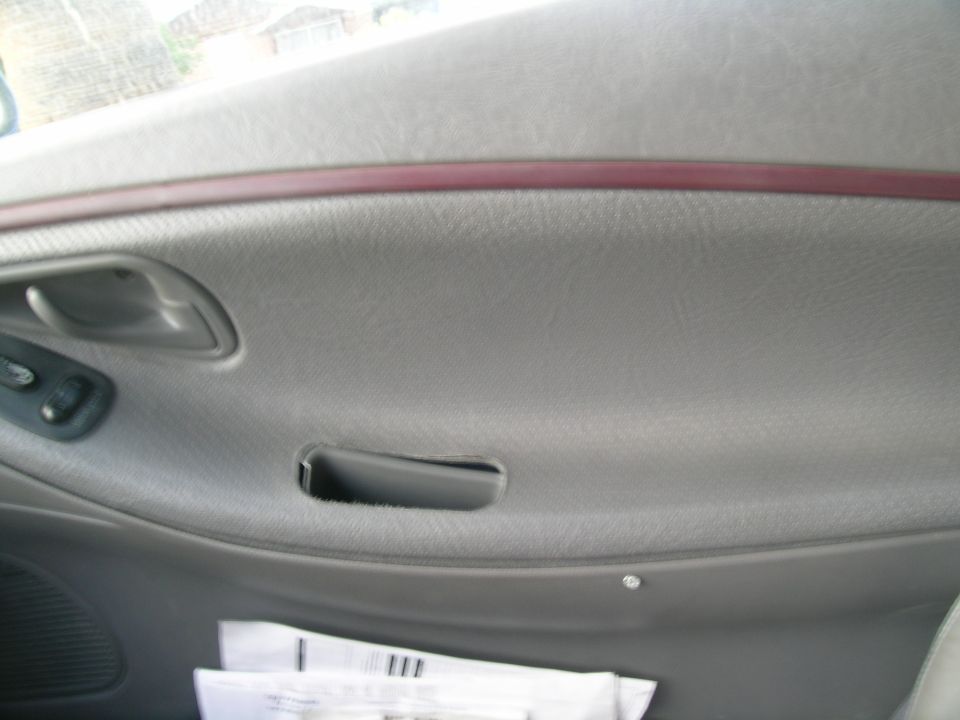 Gray car interior door panel with a red trim strip, door handle, and window controls. Papers are visible in the lower section