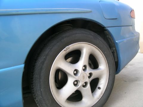 1995 Ford Probe - The rear wheel and fender of a blue 1995 Ford Probe are visible in this close-up shot.