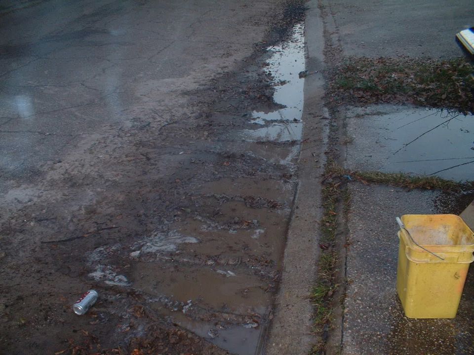Muddy runoff and a yellow bucket along a residential curb