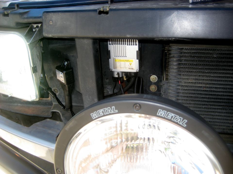 Close-up of a vehicle's front-end lighting system, showing a headlight, ballast, and wiring