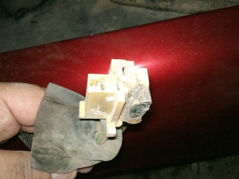 1998 Ford Crown Victoria - Close-up of a damaged blower motor resistor connector, likely from a vehicle, against a red metallic surface.