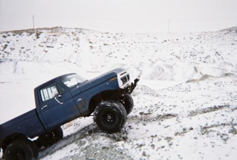 1976 Ford F-100 - A modified blue pickup truck navigates a snowy, off-road terrain.