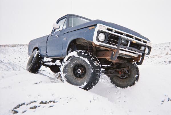 Blue 1976 Ford F-100 with large tires driving in snow
