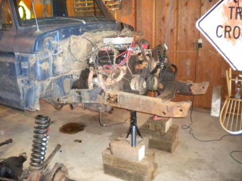 1976 Ford F-100 - The front end of a blue pickup truck is disassembled, with the engine removed and the chassis supported by jack stands.