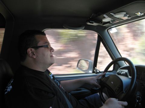 1986 Ford Bronco - A driver's perspective from inside a vehicle, with trees blurring past the window.