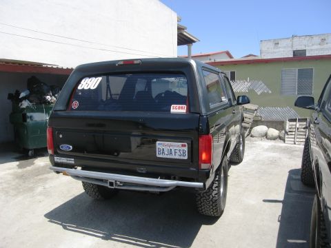 1986 Ford Bronco - This 1986 Ford Bronco features a custom rear bumper and off-road tires, seen parked next to another vehicle.