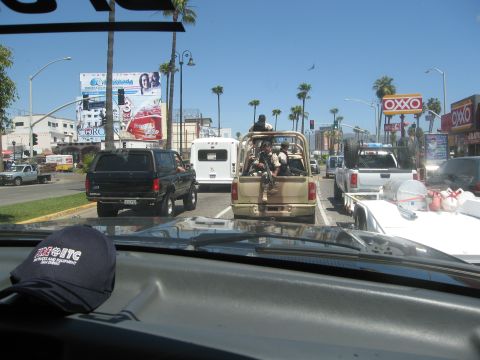 1986 Ford Bronco - A black SUV is seen from behind in a traffic jam on a sunny day with palm trees and billboards.