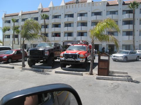 1986 Ford Bronco - Two pickup trucks and a sedan are parked in front of a white building with balconies.