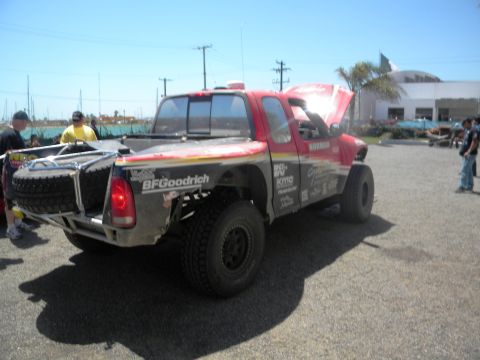 1986 Ford Bronco - A modified red pickup truck with racing decals sits parked outdoors under a clear sky.
