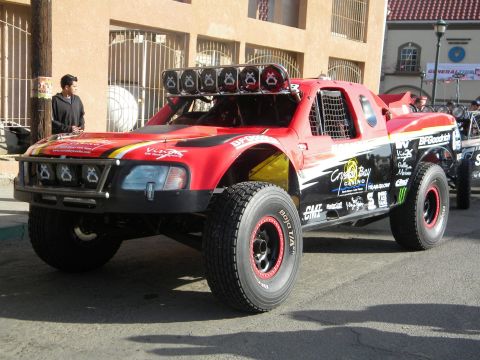 1986 Ford Bronco - A modified off-road truck with racing decals is parked on a street, with another vehicle visible behind it.