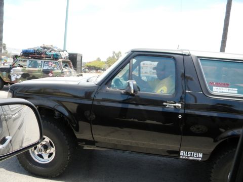 1986 Ford Bronco - Side view of a black 1986 Ford Bronco, with a camouflaged vehicle in the background.