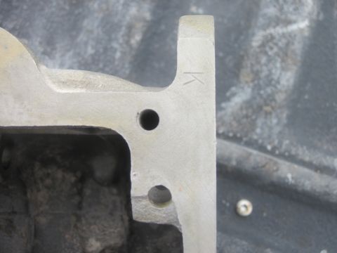 1979 Ford Bronco - Close-up of a metal engine component a stamped 'K' and two circular openings.