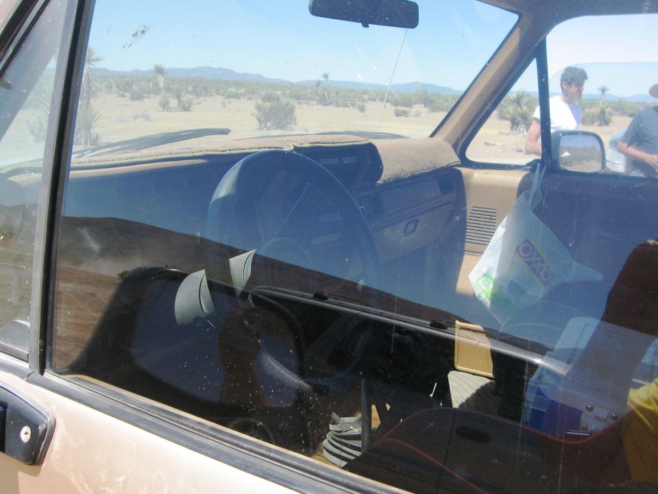 1986 Ford Bronco interior, dashboard and seats visible through dusty windshield, desert landscape outside