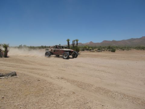 1986 Ford Bronco - A custom off-road buggy navigates a dusty desert terrain under a clear blue sky.
