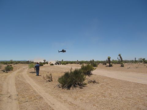 1986 Ford Bronco - A helicopter flies over a desert landscape with off-road vehicles and a person on a dirt track.