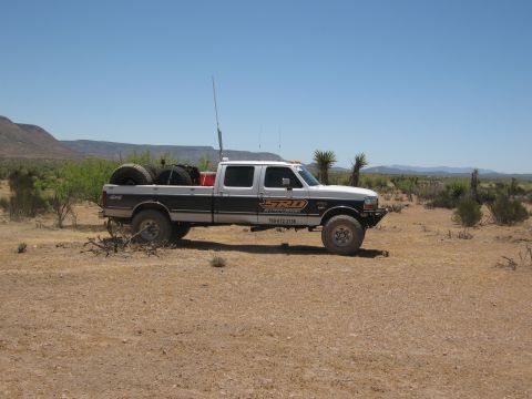 1986 Ford Bronco - A white and grey Ford F-250 Super Duty pickup truck is parked in a desert environment under a clear blue sky.
