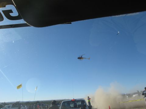 1986 Ford Bronco - A helicopter flies in the sky above a dusty desert scene with several vehicles and people gathered below.