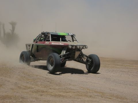 1986 Ford Bronco - A custom off-road buggy races across a dusty desert landscape, its wheels churning up a cloud of dirt.