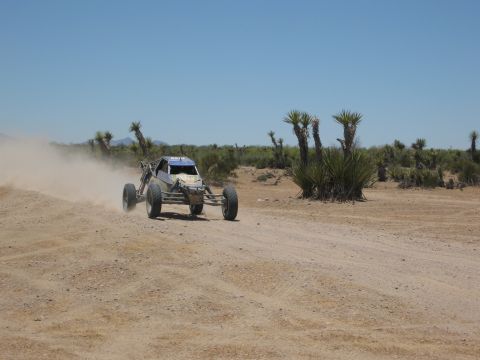 1986 Ford Bronco - An off-road buggy races across a dusty desert track under a clear blue sky.