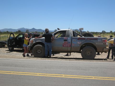 1986 Ford Bronco - A group of people gather around a modified off-road truck, possibly during a race event.