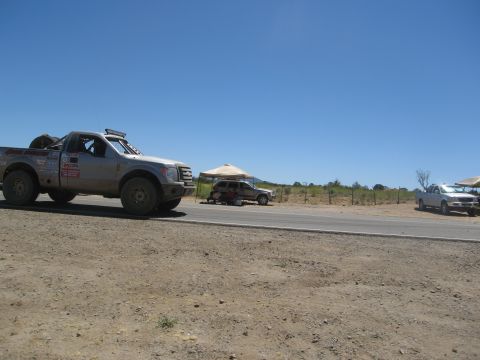 1986 Ford Bronco - A modified pickup truck sits on the side of a road under a clear blue sky, with other vehicles nearby.