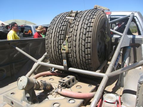 1986 Ford Bronco - Spare tires are secured within a roll cage, with other vehicles visible in the background.