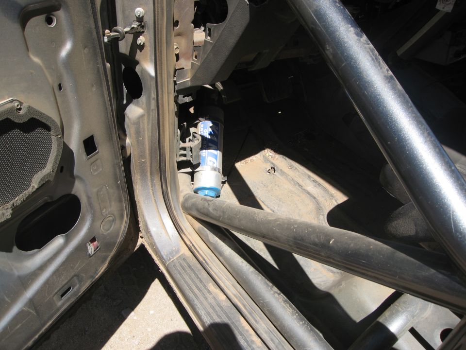 Inside view of a vehicle's door frame, showing a roll cage and a blue canister. The door panel is removed