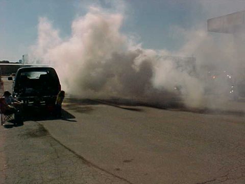 1991 Ford Bronco - A dark pickup or SUV doing a burnout in a paved lot, laying down black rubber marks as a huge cloud of white tire smoke billows across the…