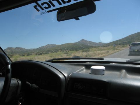 1986 Ford Bronco - View from inside a vehicle shows a dashboard and a distant pickup truck on a road with mountains in the background.