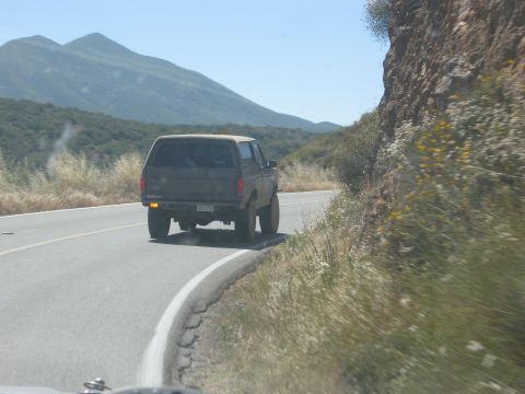 1986 Ford Bronco - A 1986 Ford Bronco navigates a scenic, winding mountain road under a clear blue sky.