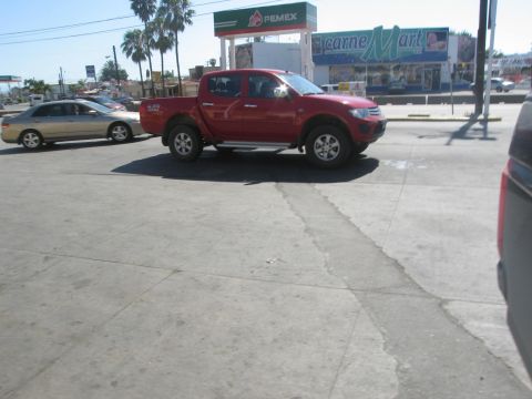 1986 Ford Bronco - A red pickup truck is parked on a paved surface near a gas station and a store.