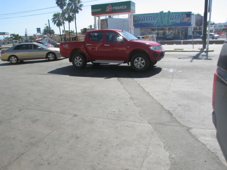 Red pickup truck parked next to a silver sedan, with a PEMEX gas station and Carne Mart in the background