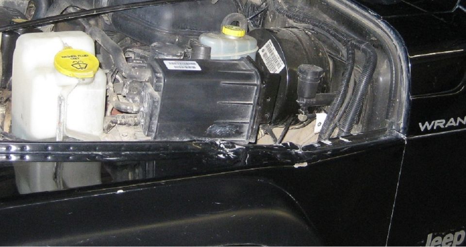 Charcoal canister and reservoirs in the engine bay of a black Jeep Wrangler