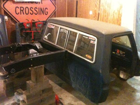1976 Ford F-100 - A truck cab and chassis sits in a garage, with a "Crossing" sign visible in the background.