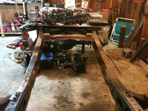 1976 Ford F-100 - Disassembled vehicle frame and engine parts are laid out on a workbench in a garage setting.
