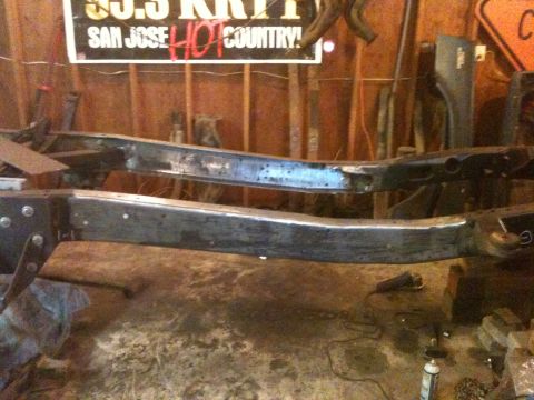 1976 Ford F-100 - The bare frame of a vehicle is shown in a workshop setting, with various tools and a sign visible.