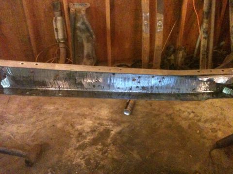 1976 Ford F-100 - A damaged metal bumper is shown in a workshop setting, with tools and parts in the background.
