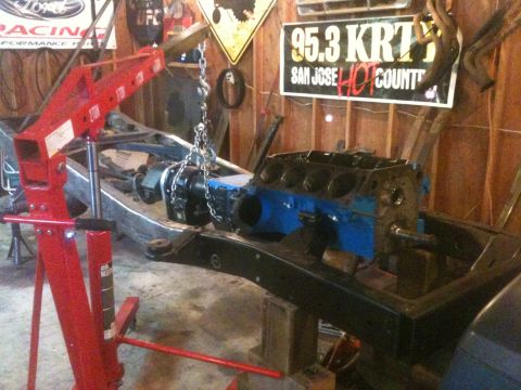 1976 Ford F-100 - Engine block and frame assembly in a workshop, with a red engine hoist ready for work.