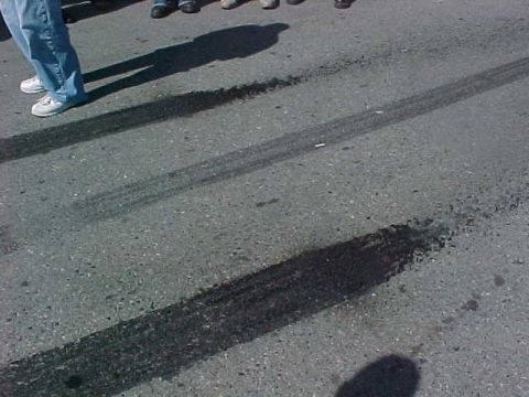 1991 Ford Bronco - Tire marks are visible on the asphalt, with several people standing in the background.