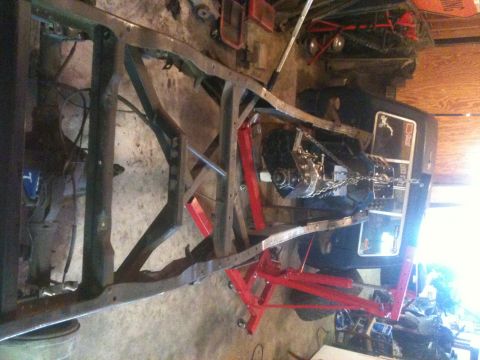1976 Ford F-100 - Truck frame and drivetrain assembly, likely undergoing restoration or modification, with a red engine hoist in place.