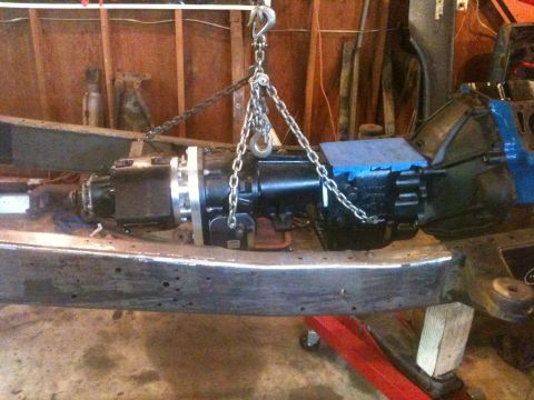 1976 Ford F-100 - A transmission is suspended by chains and a hoist, ready for installation or removal from a vehicle's frame.